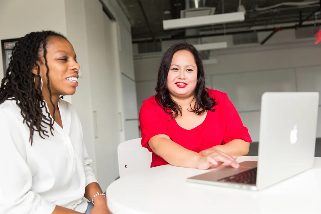 Dos mujeres adultas conversan frente a una computadora y toman notas sobre una situación financiera